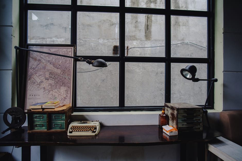 A vintage office desk setup featuring a typewriter, Paris map, and classic decor by a window.